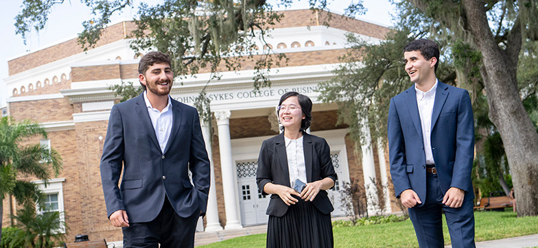Two students dressed in suits talking with a professor