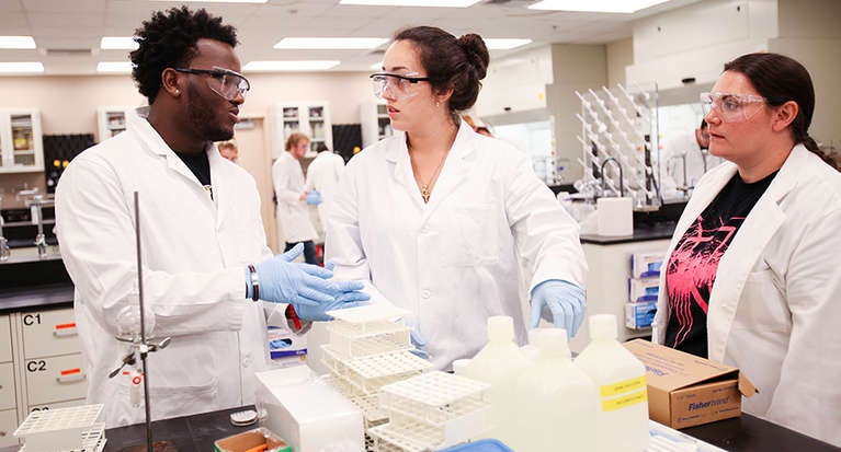 Two students and a professor talk in a chemistry lab.