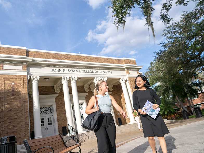 Two women walking in front of the Sykes College of Business.
